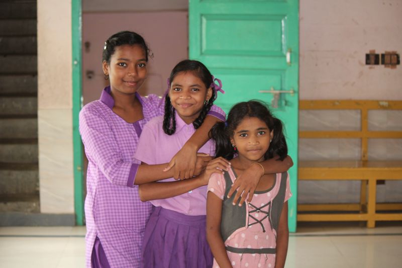 Three children standing together by a green doorway during an India mission visit