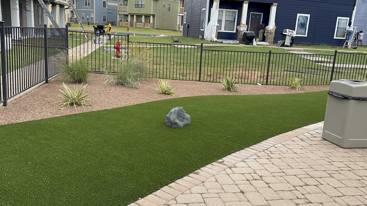 Artificial turf beside curved pavers, rock beds and black metal fencing at Cottage Row