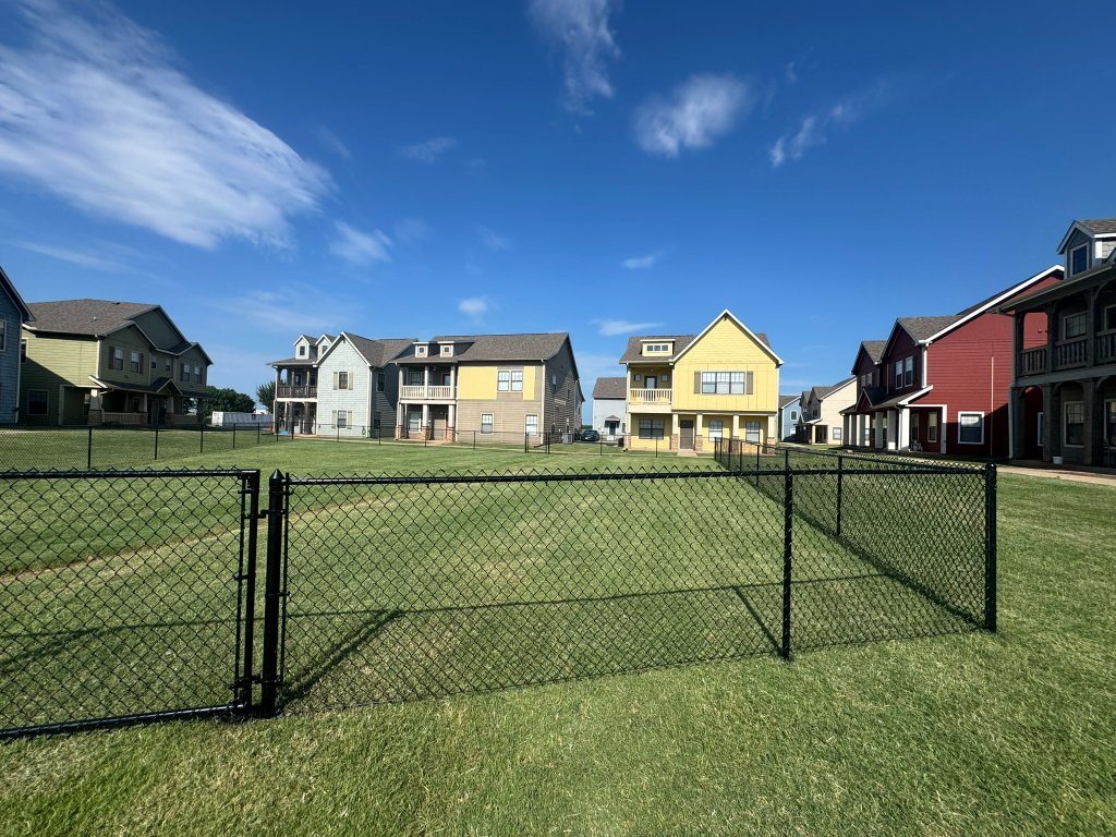 Black chain-link fencing around a natural-grass dog park at a residential community