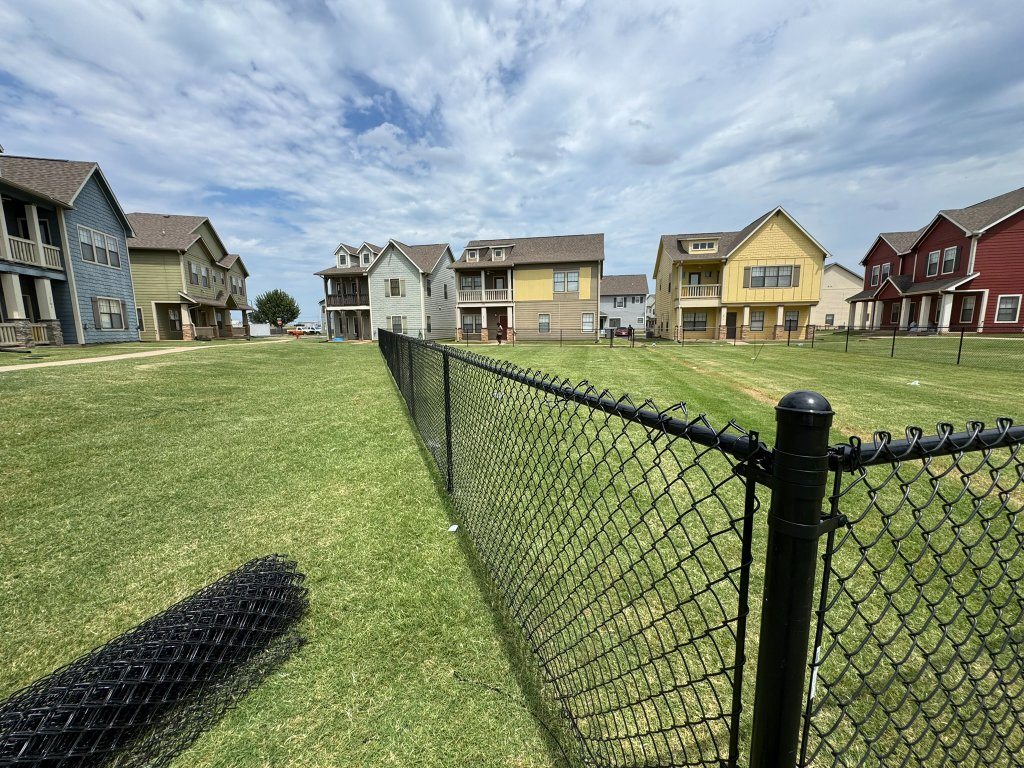 Mowed natural-grass lawn and black chain-link fence beside community homes