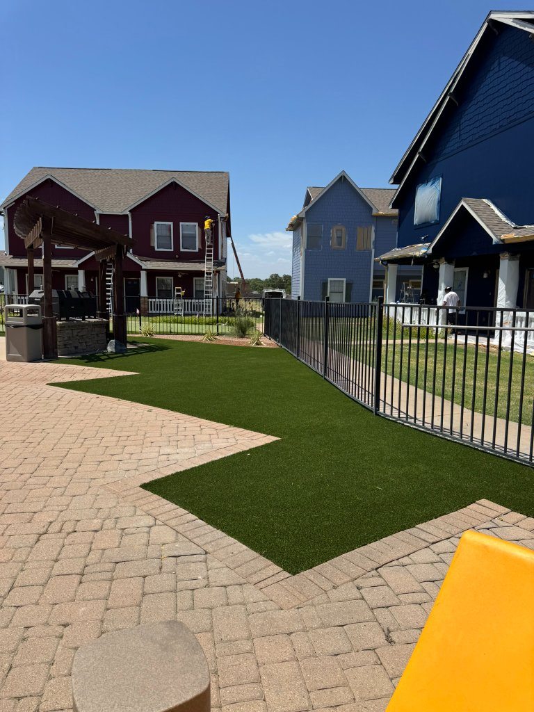 Black metal fence bordering artificial turf and pavers at Cottage Row
