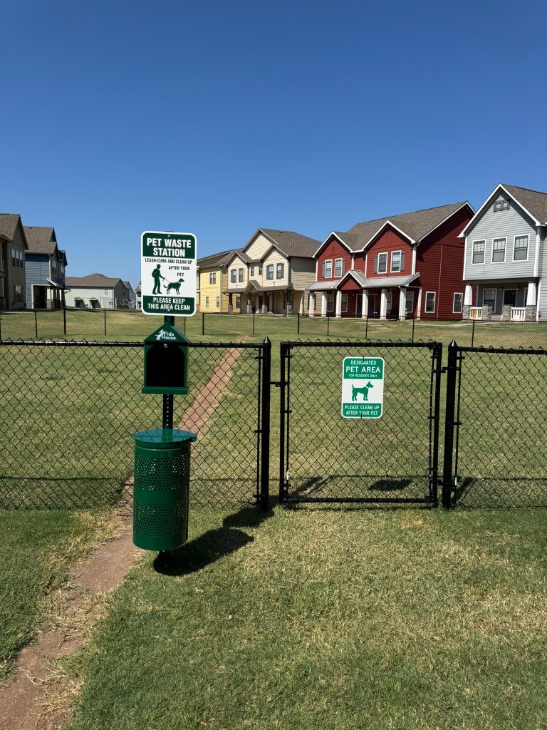 Black chain-link dog-park gate opening onto a natural-grass lawn