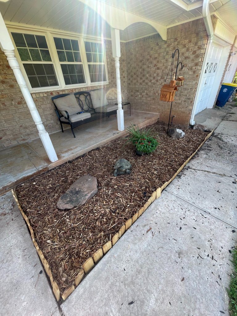 Mulched planting bed with a stone border beside a covered front porch