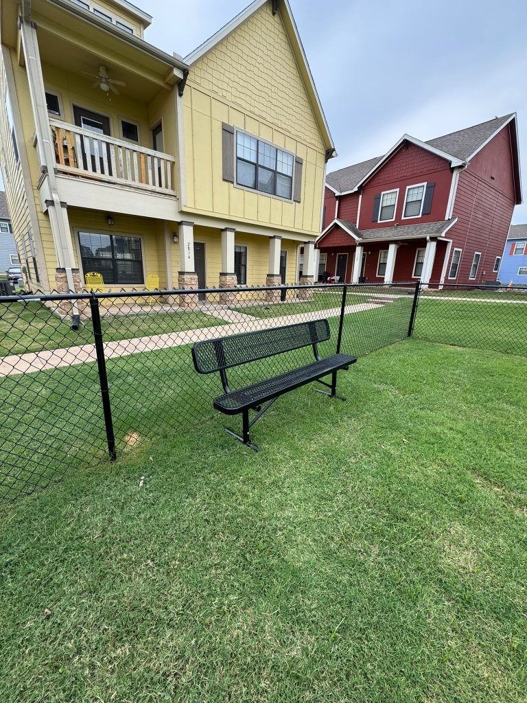 Natural-grass lawn with a bench beside black fencing and residential buildings