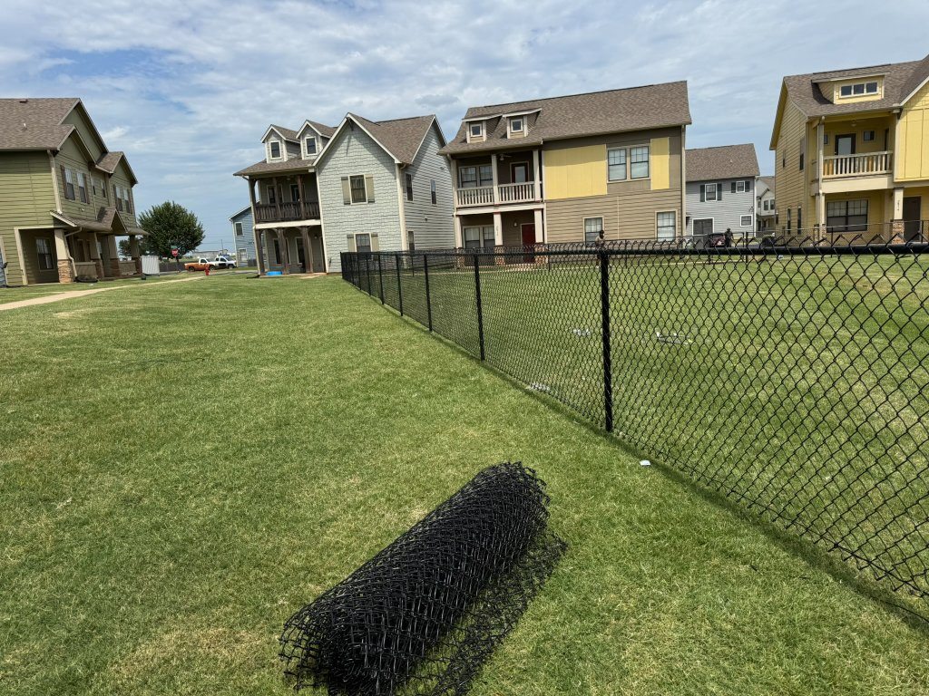 Natural-grass slope bordered by black chain-link fencing at a residential community