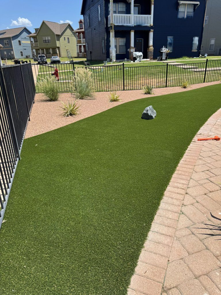 Curved artificial-turf area bordered by rock beds and pavers at Cottage Row