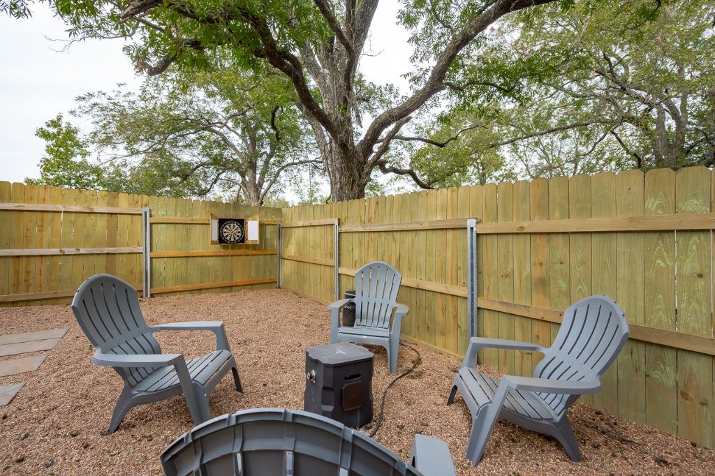 Outdoor chairs around a fire pit on gravel inside a fenced backyard