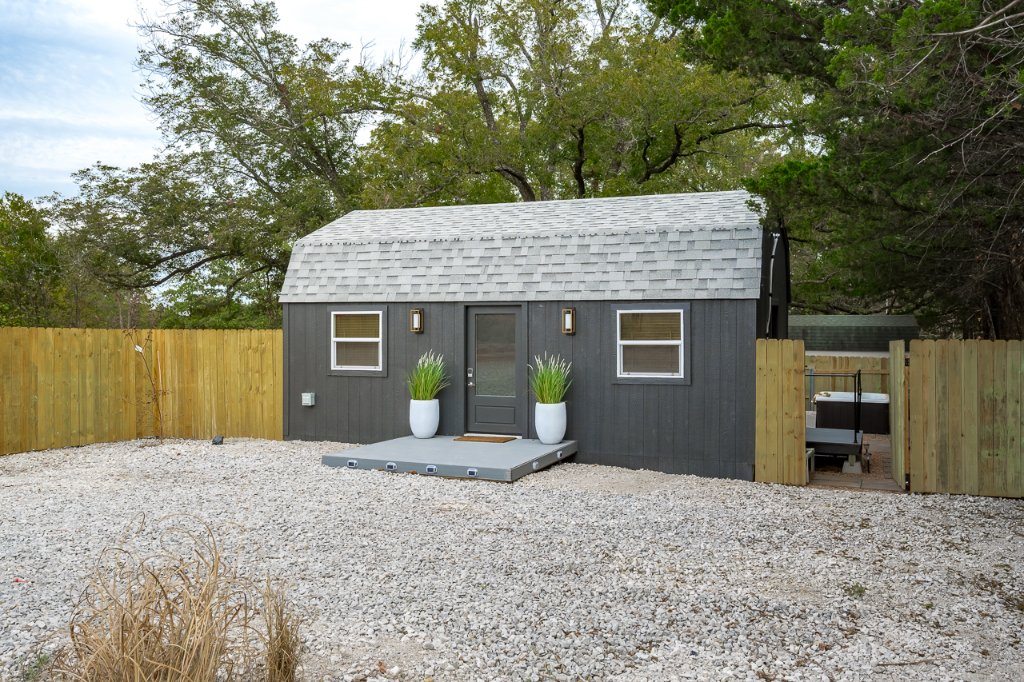 Small gray guesthouse beside a gravel yard and wood privacy fence