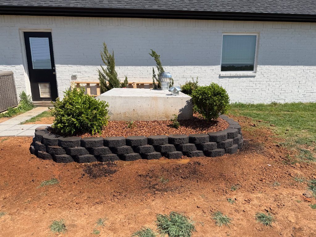 Raised planting bed edged with dark stone blocks beside a house